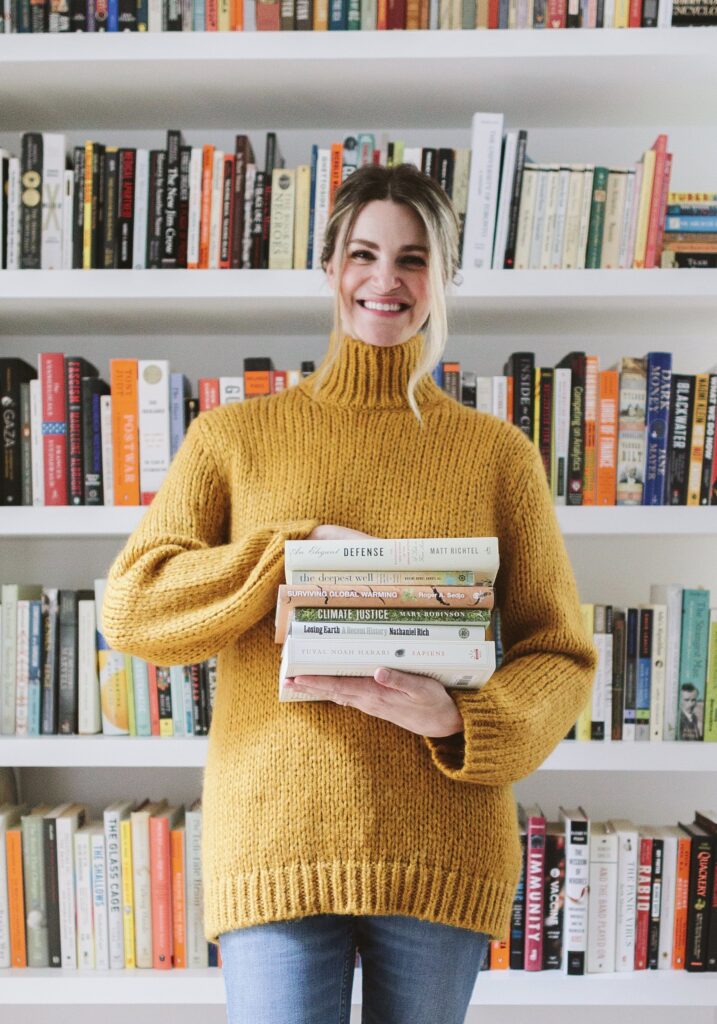 Keri West standing in front of a bookshelf holding a stack of books