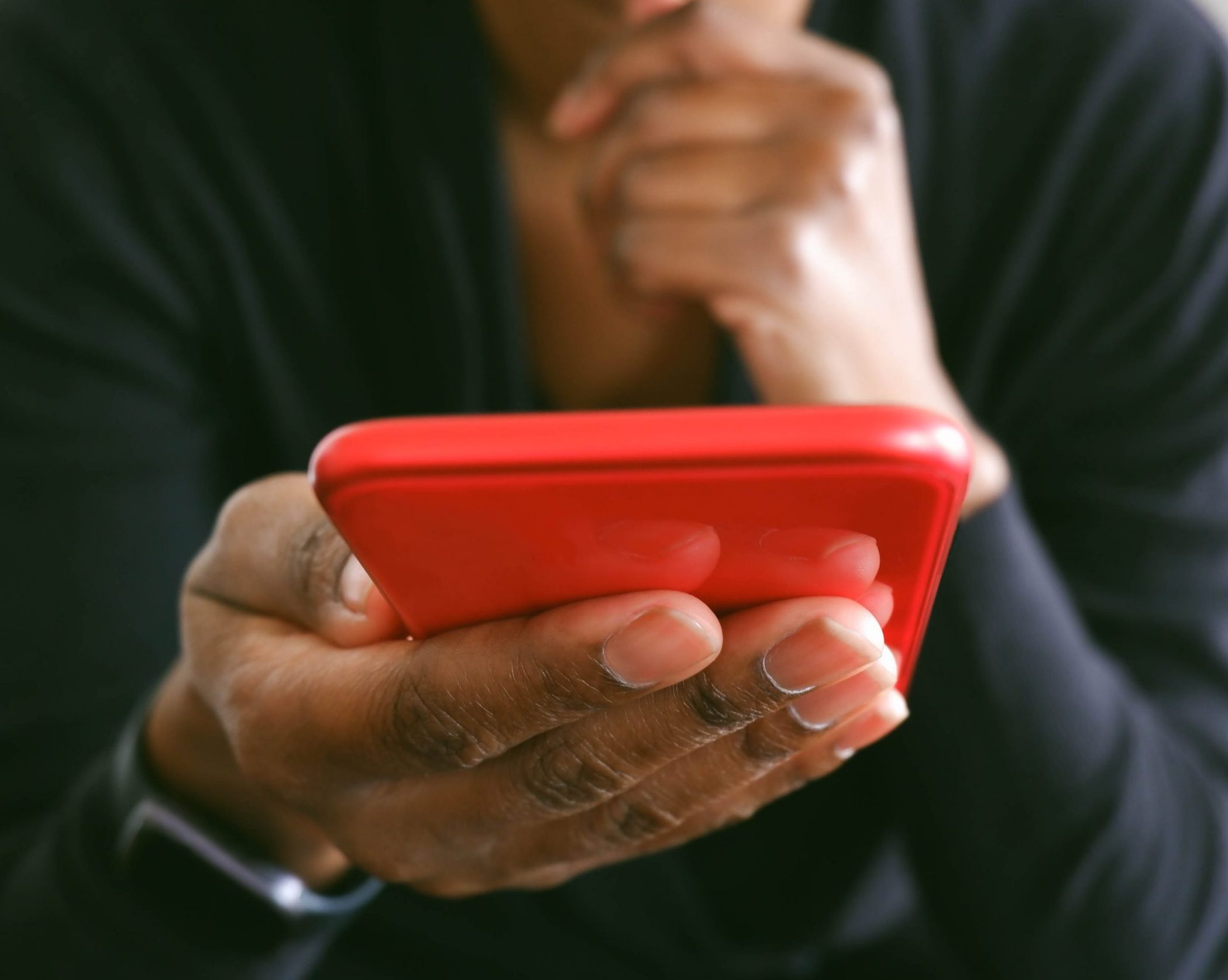 Unrecognizable black woman uses smart phone while sitting in chair in living room