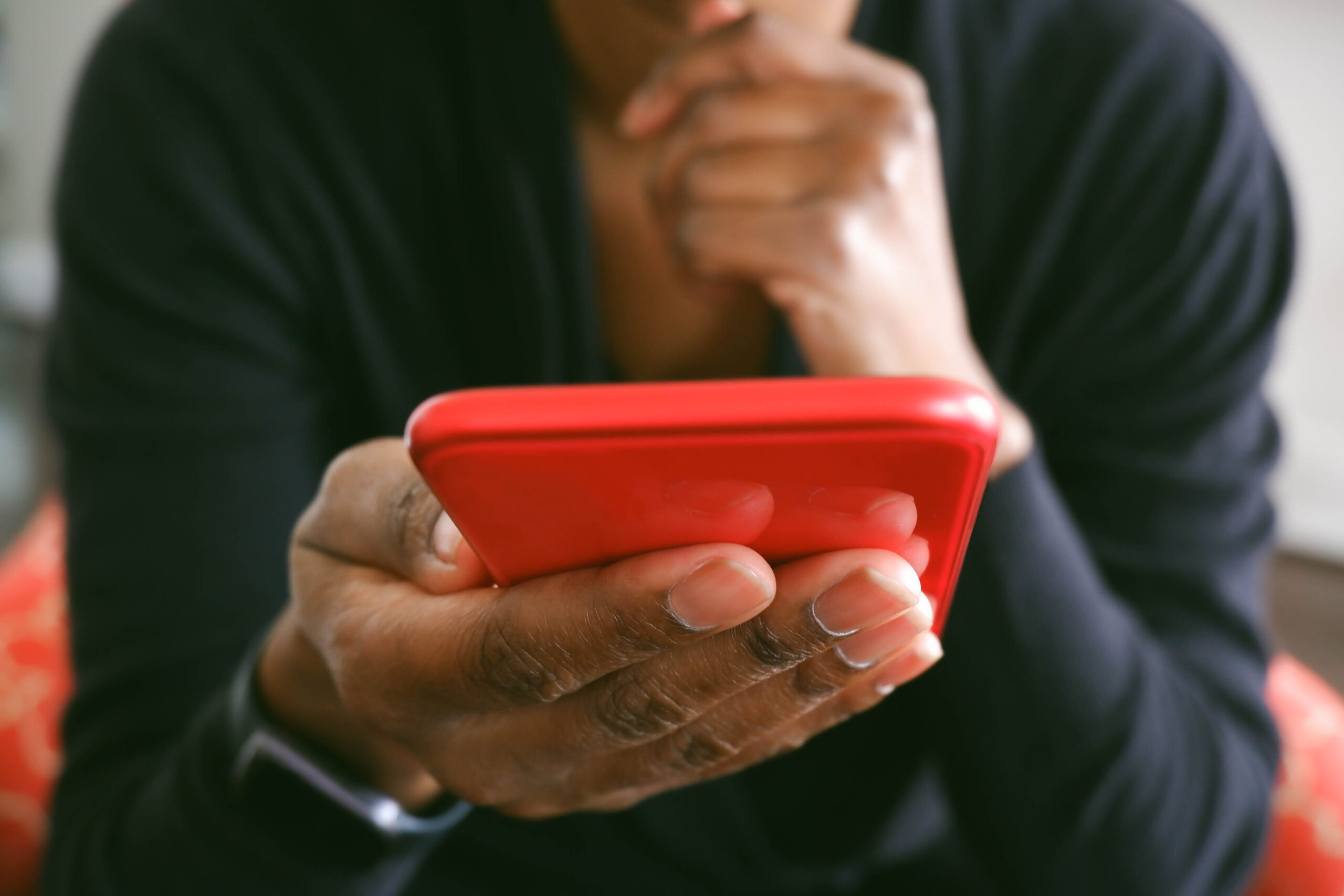 Unrecognizable black woman uses smart phone while sitting in chair in living room