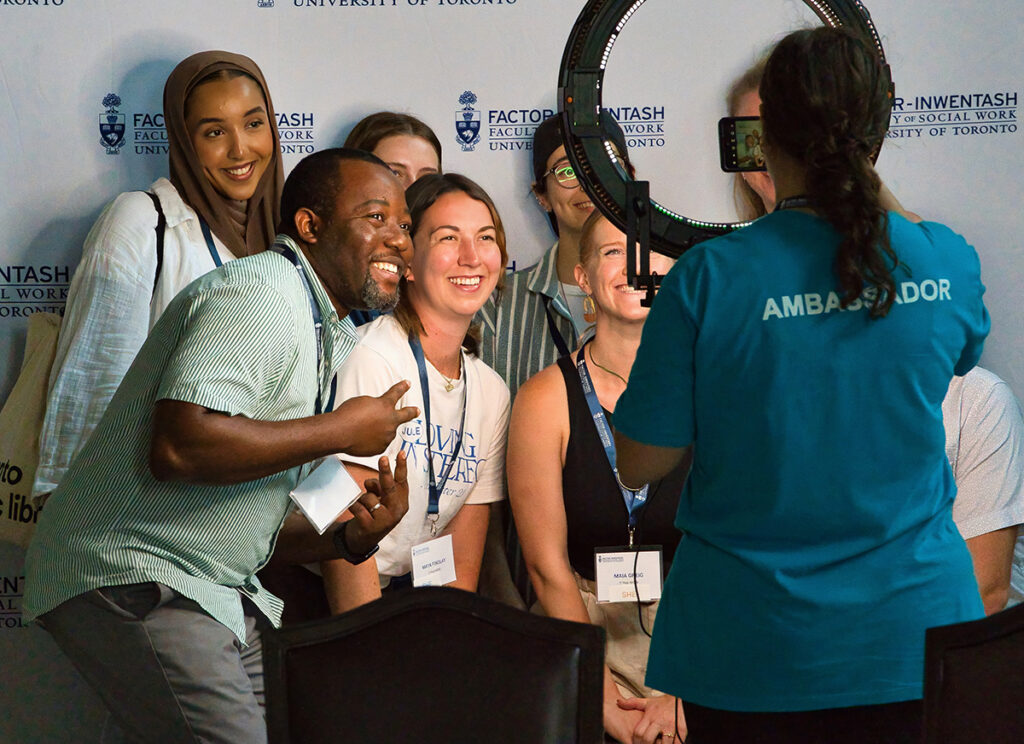 Group of new MSW students pose for a photo taken by a student ambassador in front of the FIFSW step-and-repeat