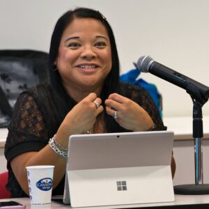 Maureen Pangan, seated and speaking with a microphone on a stand to her left