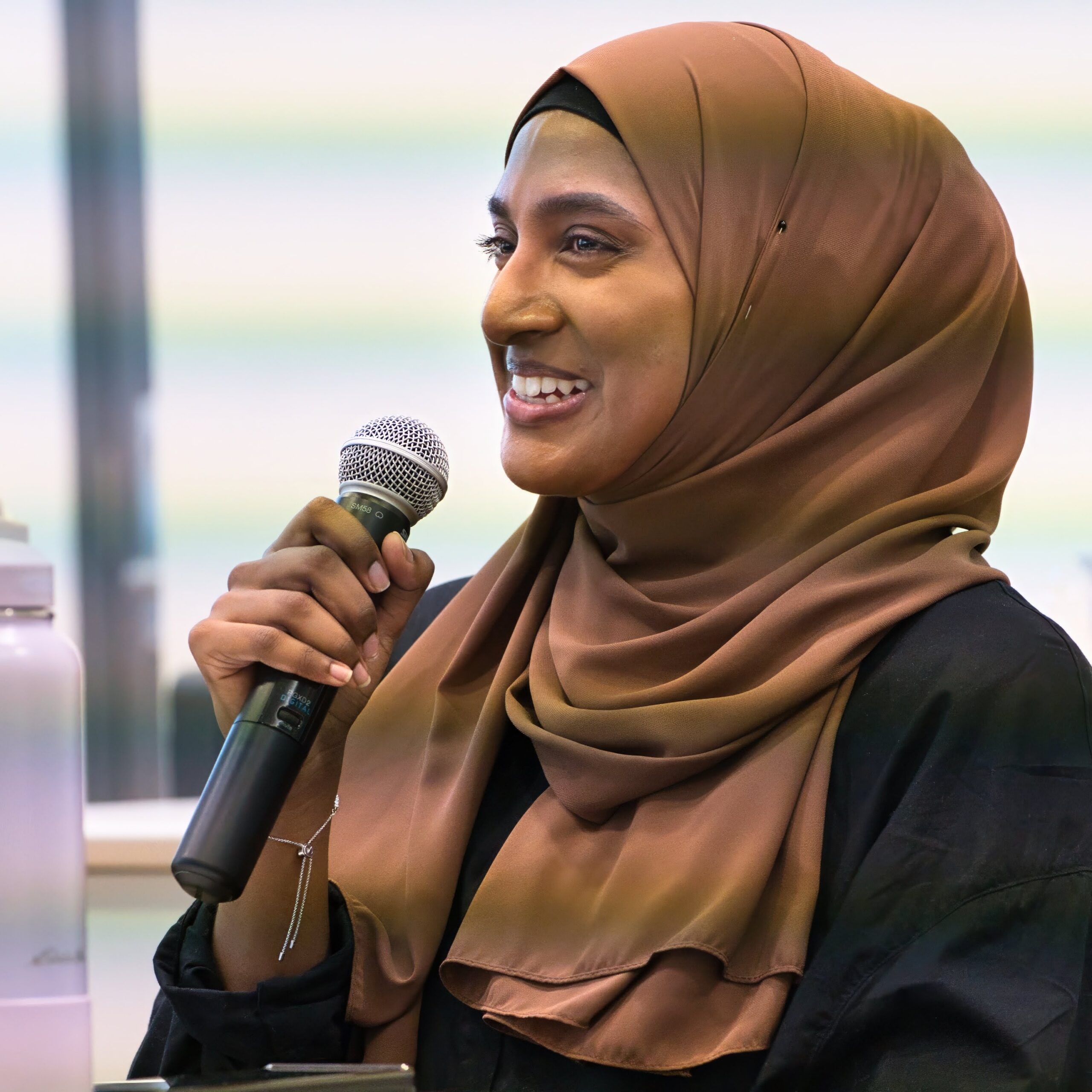 Areefah Dukhi, smiling, speaks into a microphone she is holding