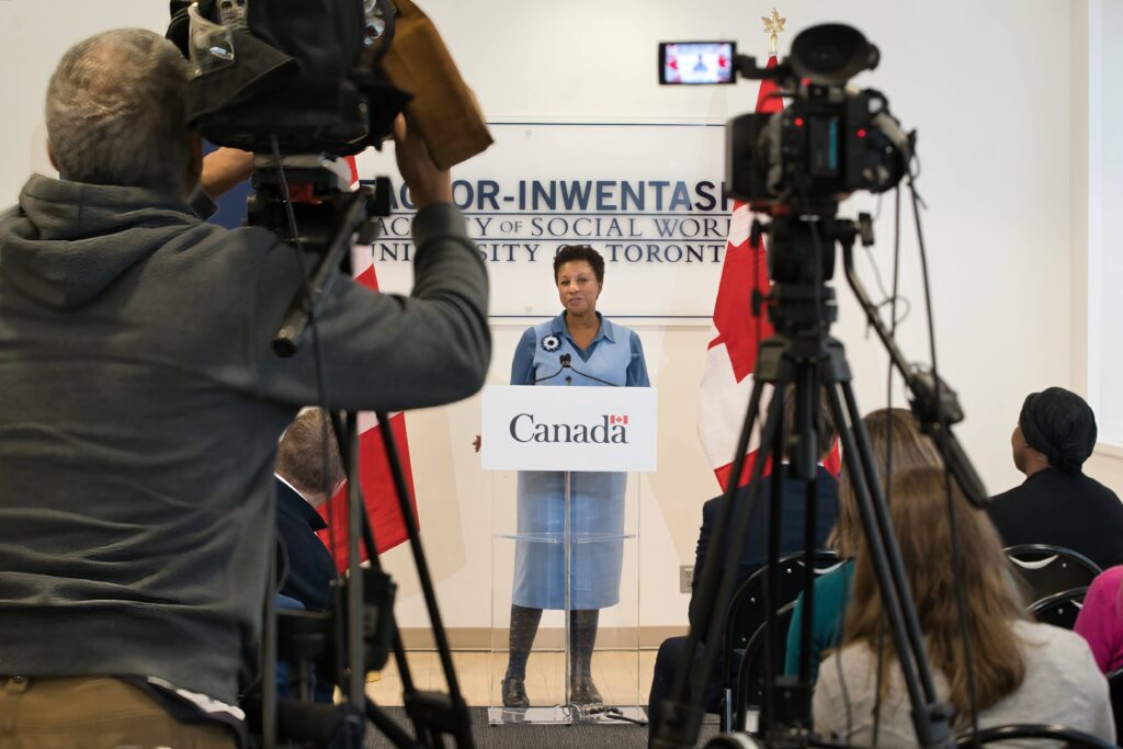 Dean Charmaine Williams speaking at the federal government announcement at podium. Media cameras in foreground