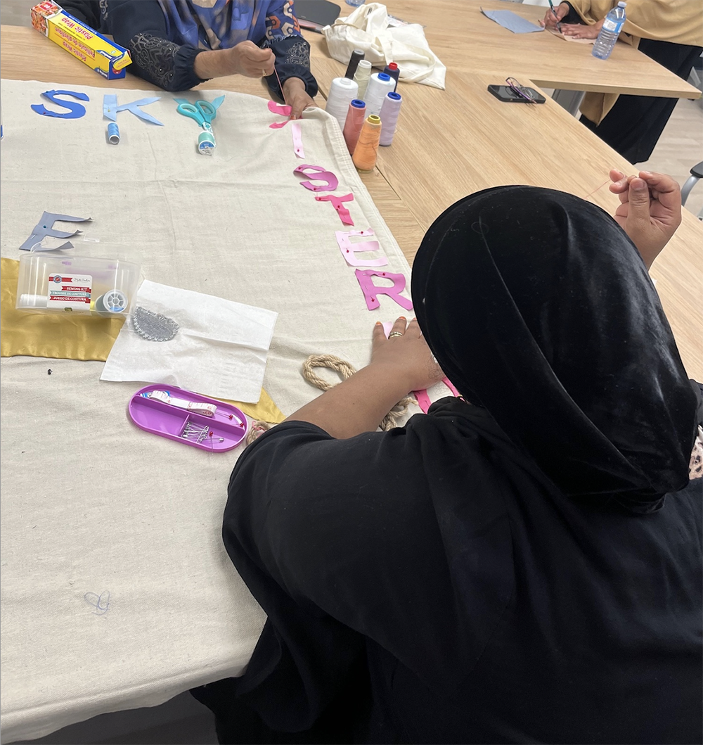 A woman in a hijab stitching sisterhood letters onto a banner