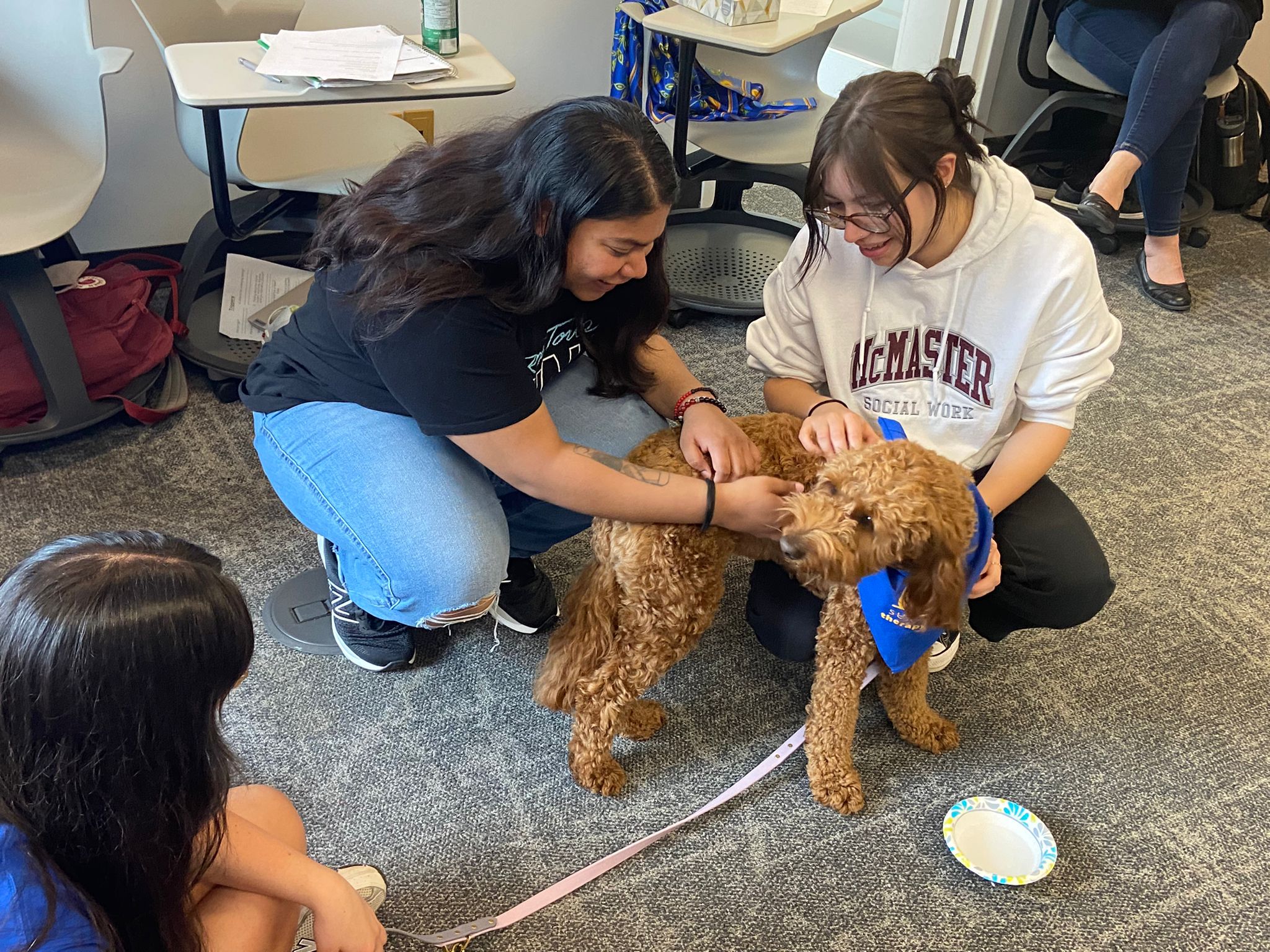 two students petting a dog in a classroom