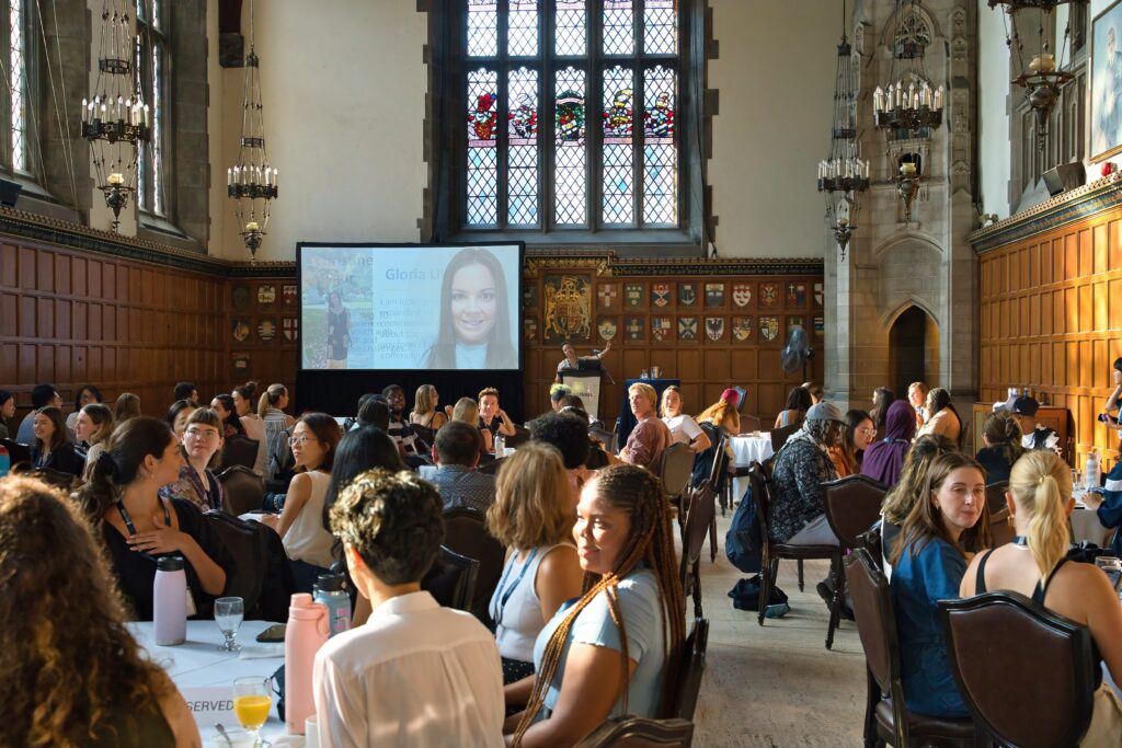 Large audience of new students siting around conference tables in Hart House during an Orientation presentation