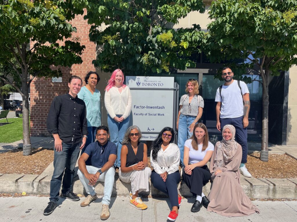 9 PhD students pose for a photo by FIFSW's sign outside its building