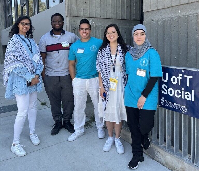 5 students stand outside next to the Tartu building and a U of T Social Work sign