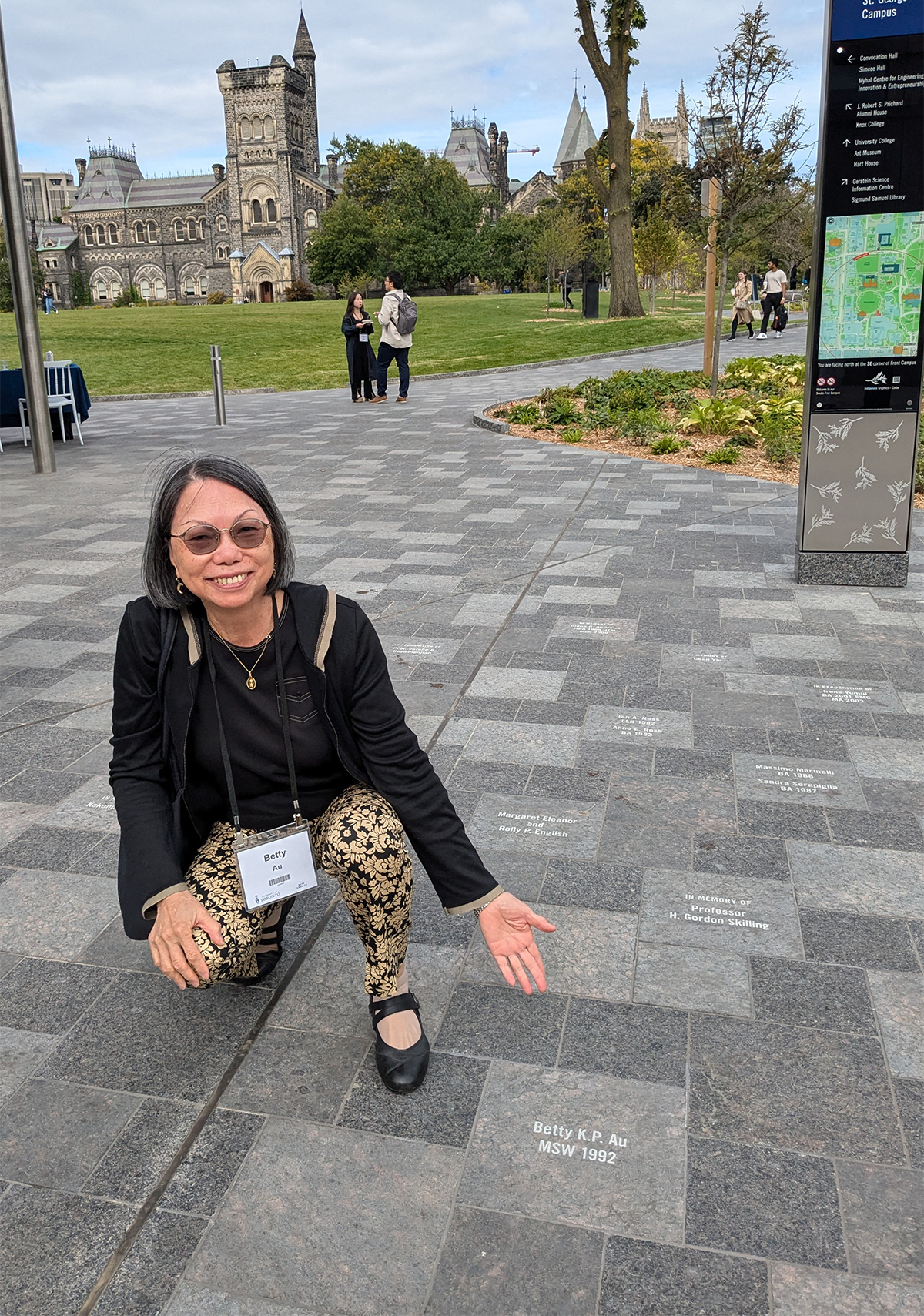 Betty Au kneeling down in front of her paver on Kings College Circle