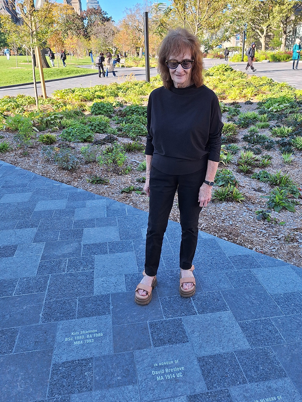 Celia Denov standing in front of and looking down at her paver dedicated to her uncle David Breedlove on Kings College Circle