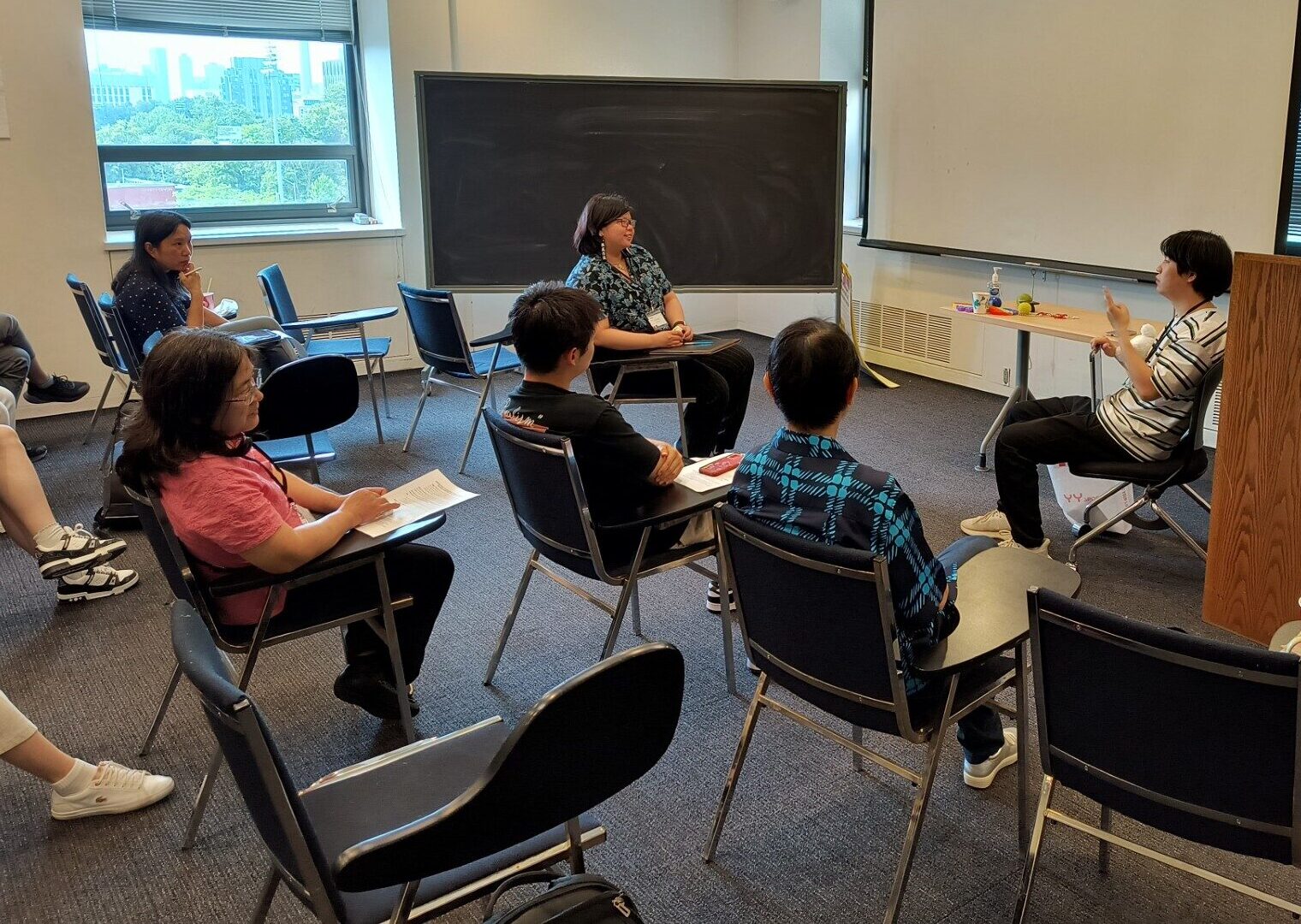 Patricia Quan, wearing glasses and a dark blue buttoned shirt with flowers listens to a participant during a storytelling forum in a classroom at FIFSW.