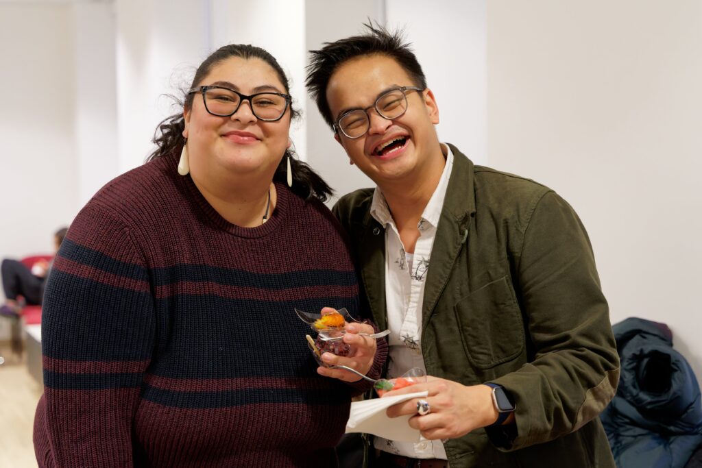 two students, standing, holding food and smiling 