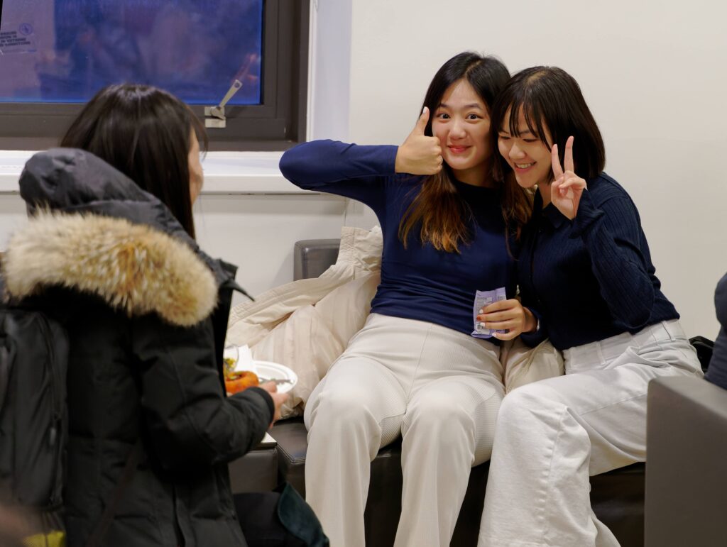 One student gives a thumbs up, another holds two fingers up in a peace sign, smiling.