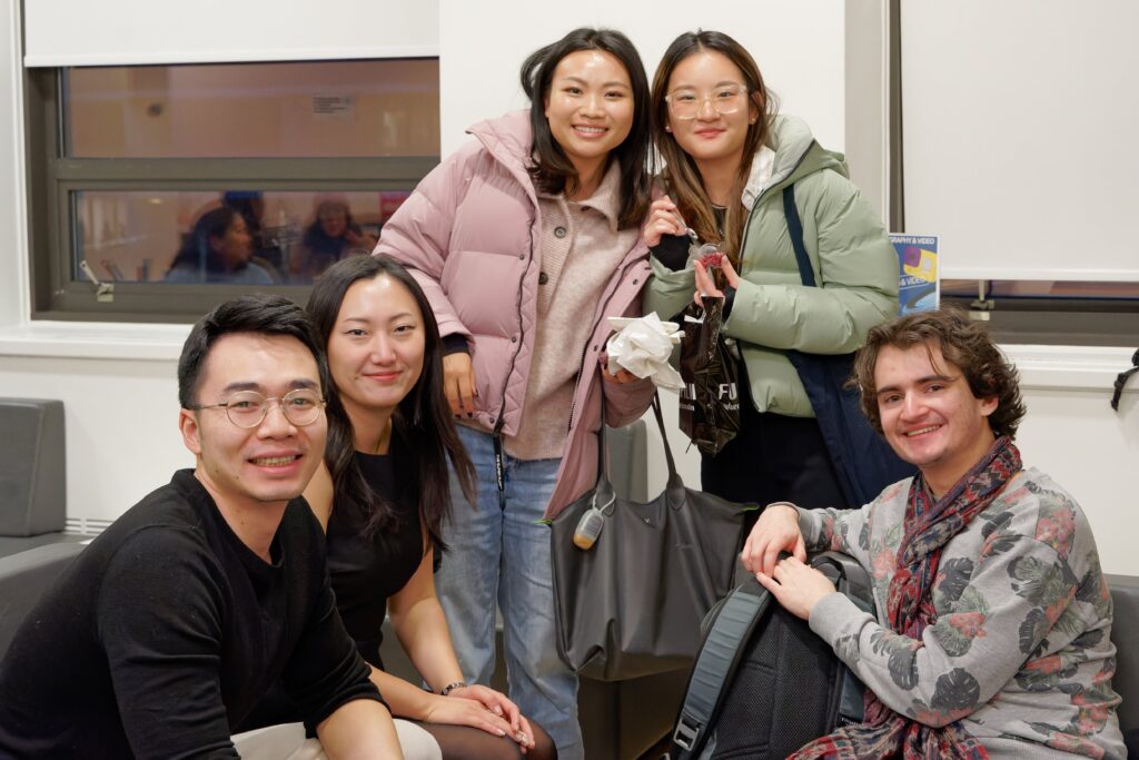 5 students, three sitting, two standing smile for the camera at a gathering in the student lounge