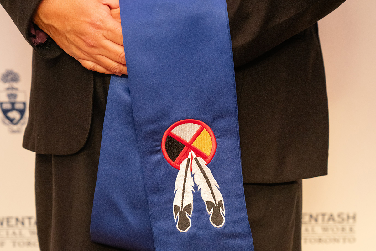 Close up of blue stole worn by graduates at convocation, featuring an embroidered medicine wheel and eagle feathers