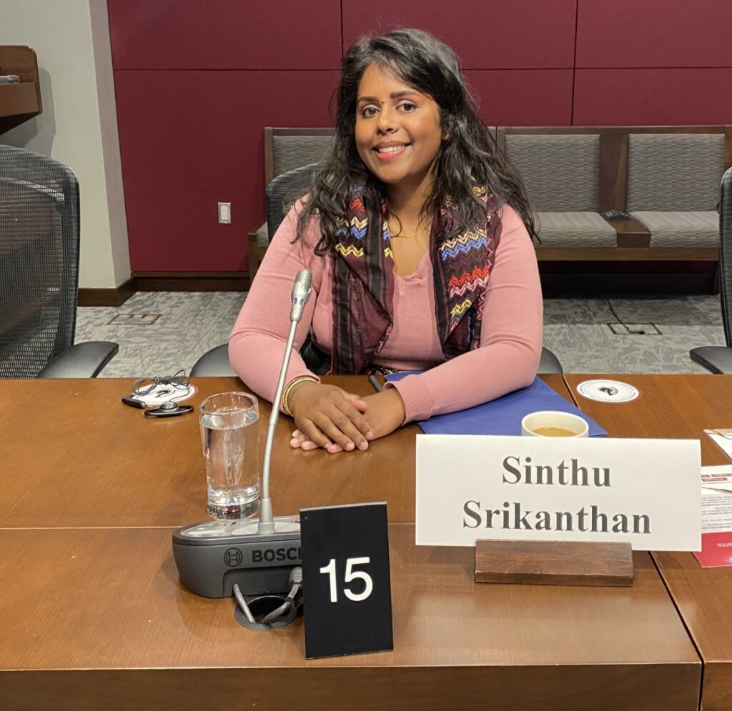 Sinthu Srikanhan poses for a photo at the Senate board hearing, sitting behind a microphone and name card at the table where she gave her testimony